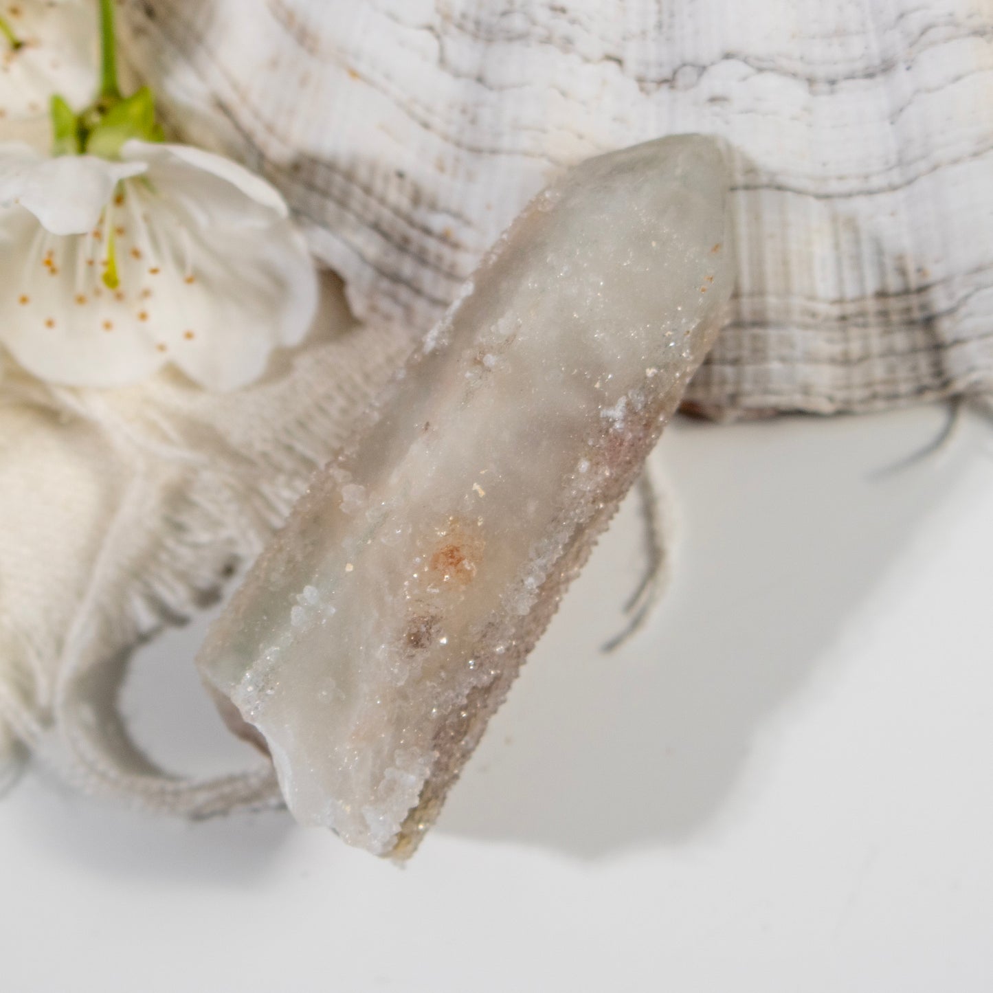 Close-up of a geode crystal with a white flower and textured fabric in the background