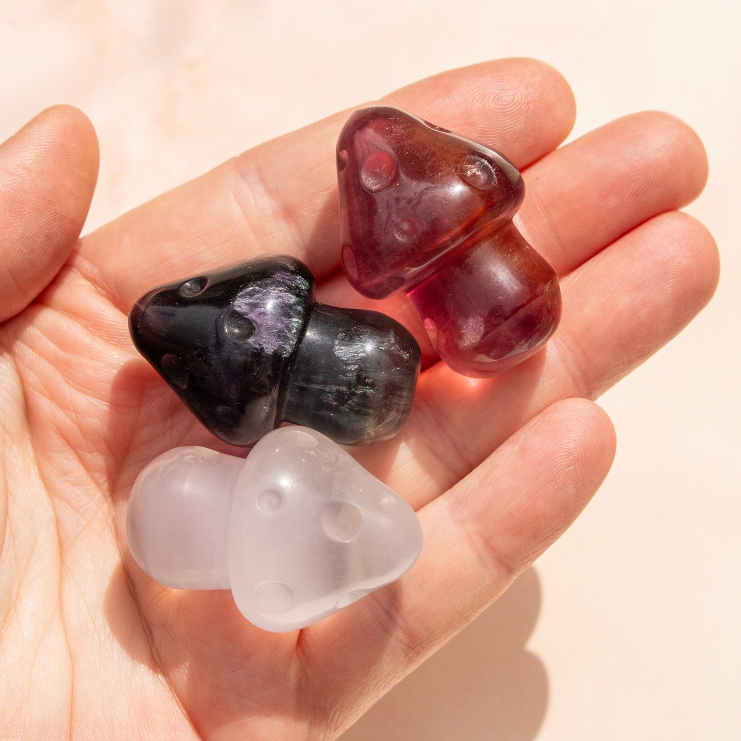 Hand holding three mushroom-shaped stones of different colors on a light background