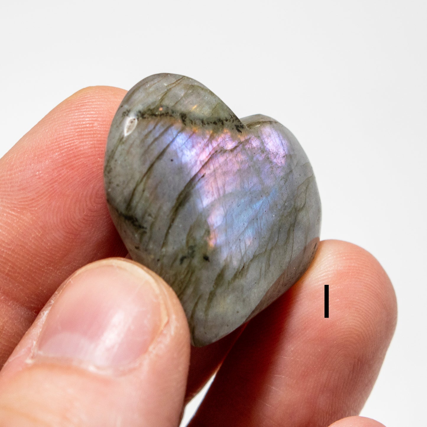 Heart-shaped labradorite stone held between fingers against a white background