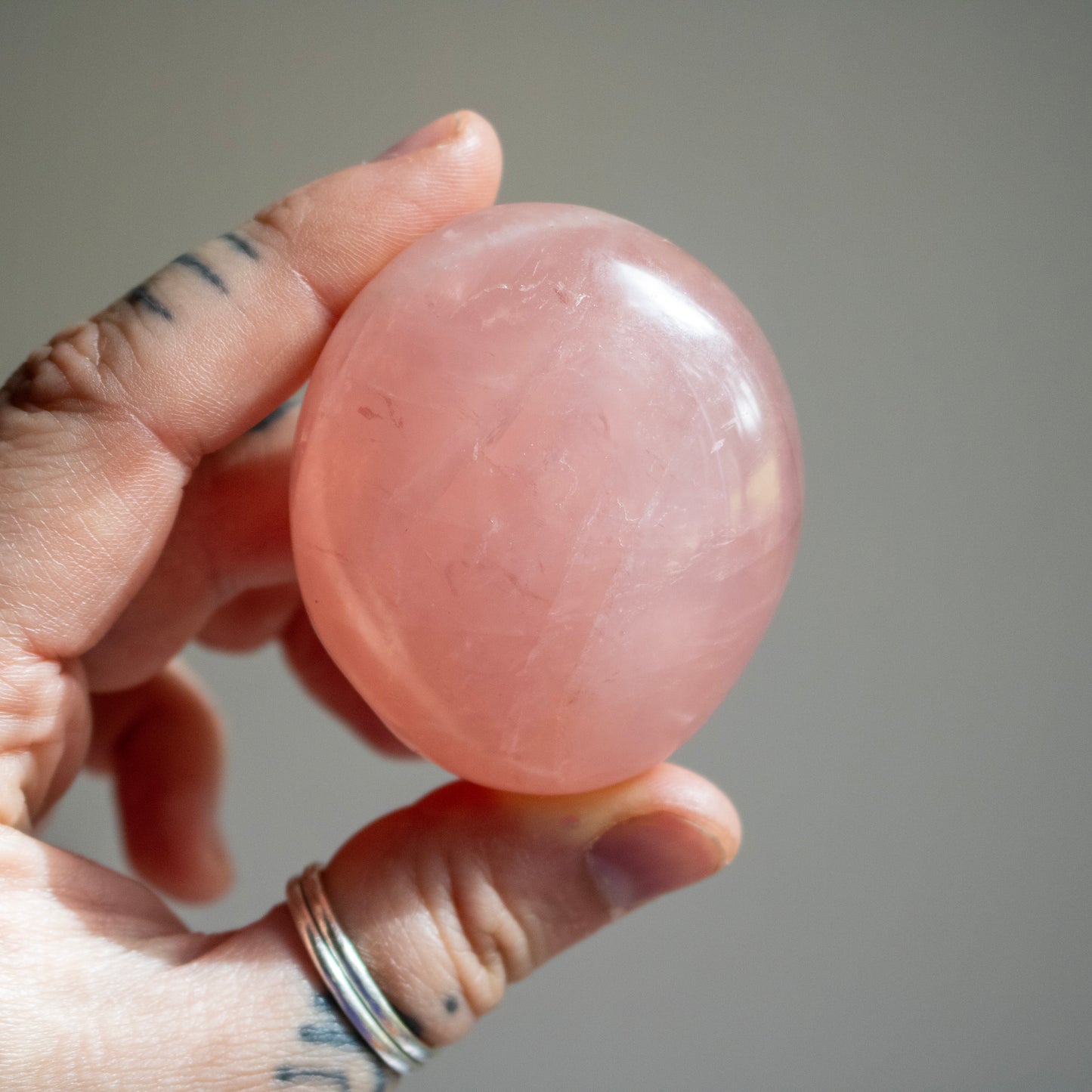 Hand holding a pink stone against a neutral background