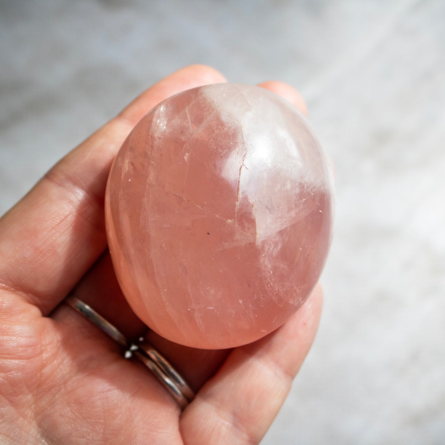 Hand holding a pink crystal stone against a neutral background