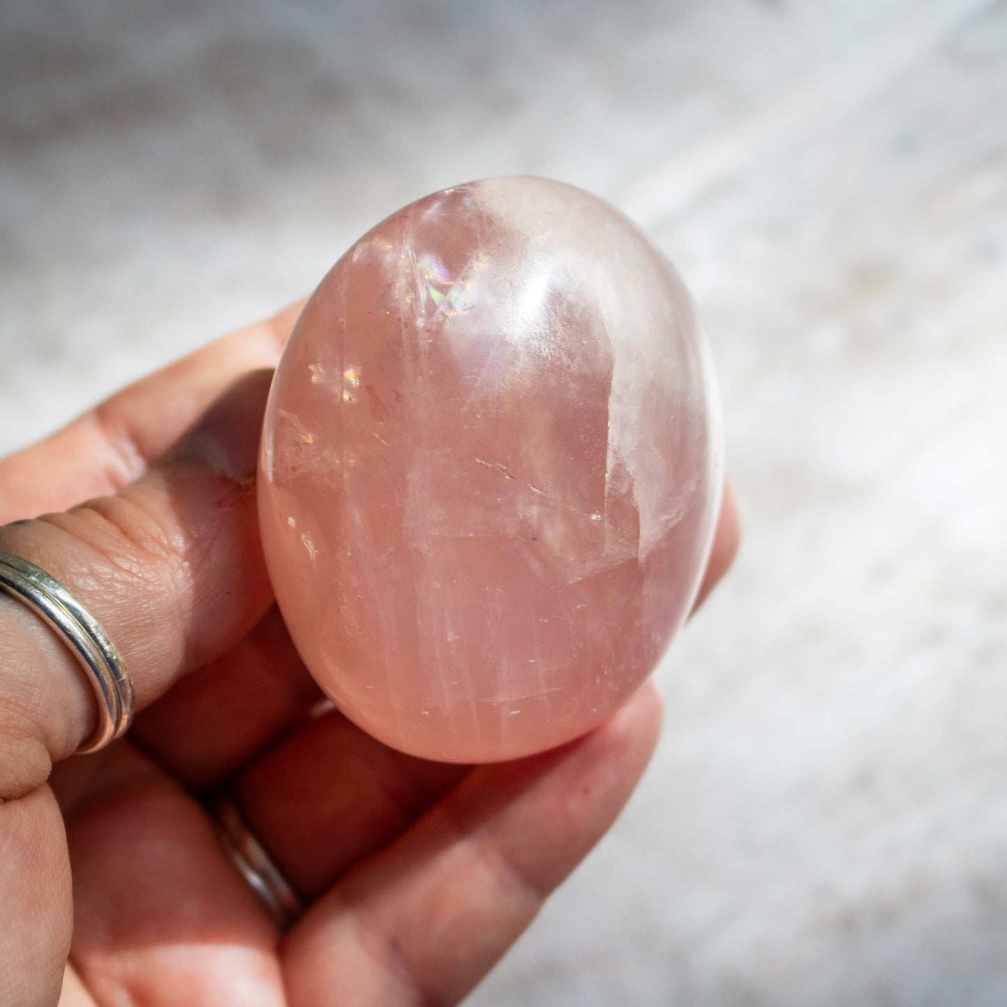Hand holding a pink crystal stone against a neutral background