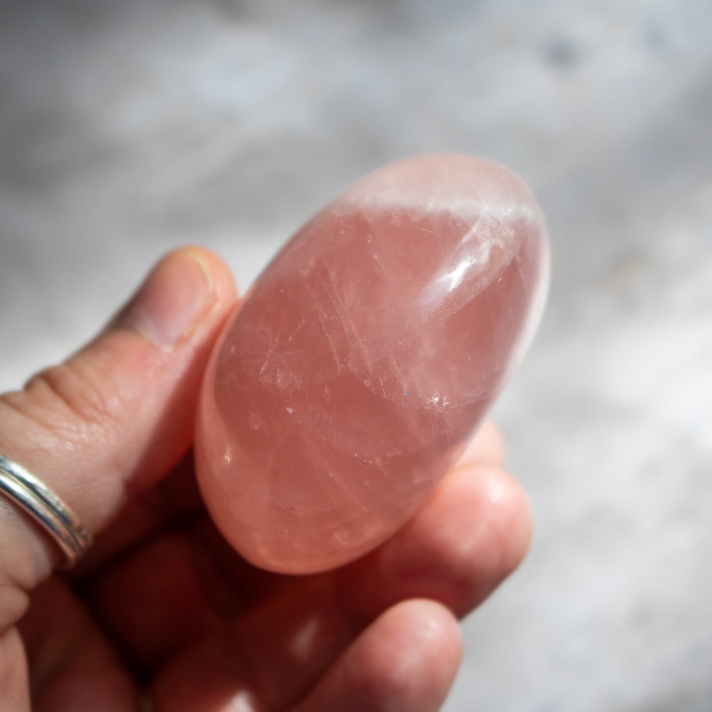 Hand holding a pink crystal against a blurred background