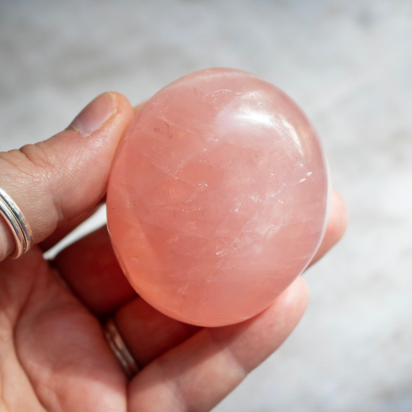 Hand holding a pink stone against a neutral background