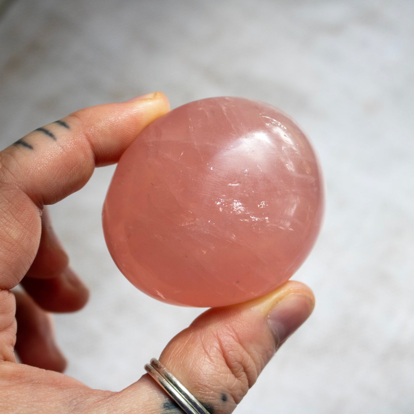 Hand holding a pink crystal ball against a neutral background