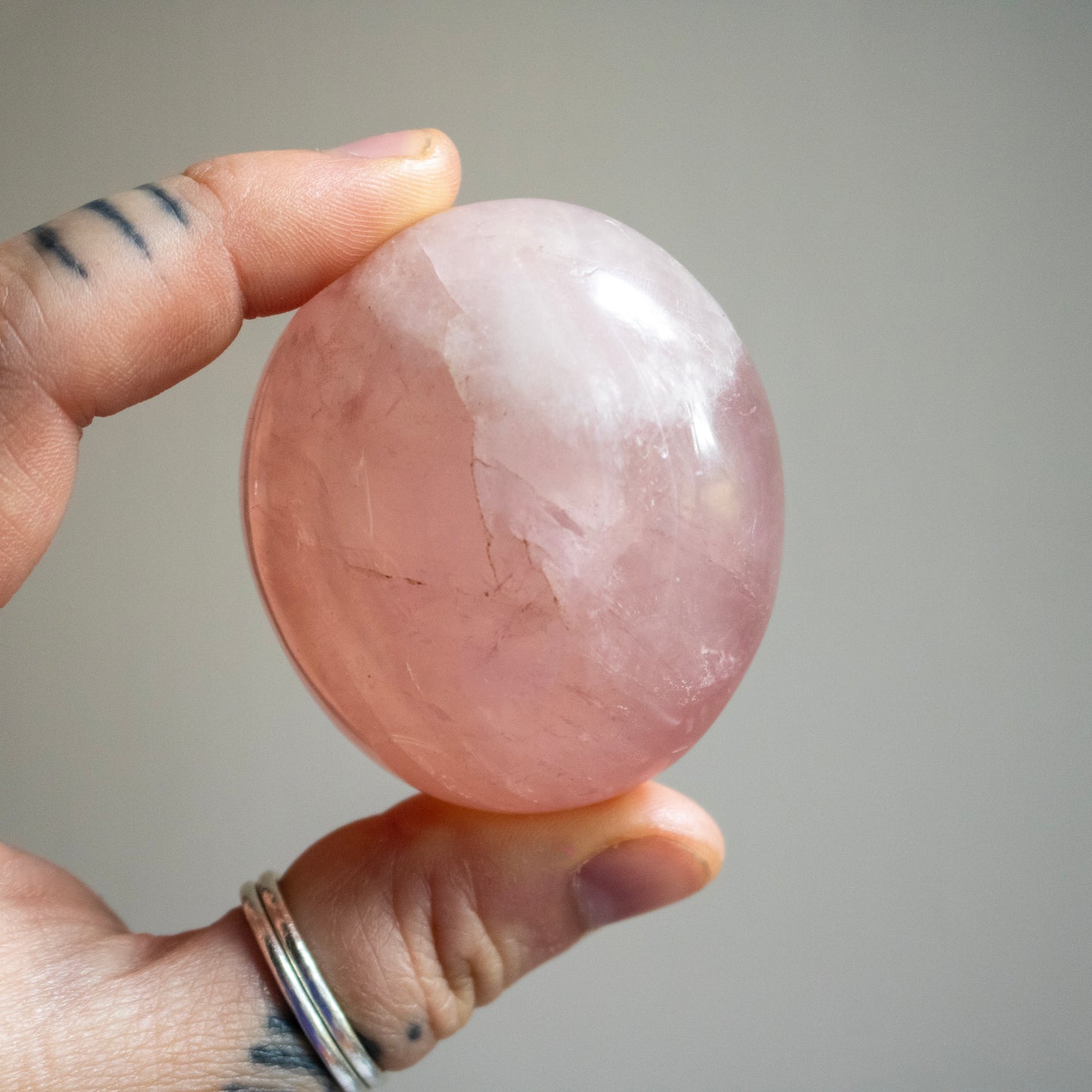 Hand holding a pink crystal ball against a neutral background