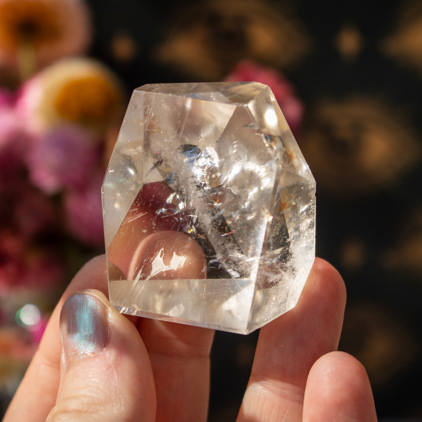Clear crystal held in a hand with a blurred floral background