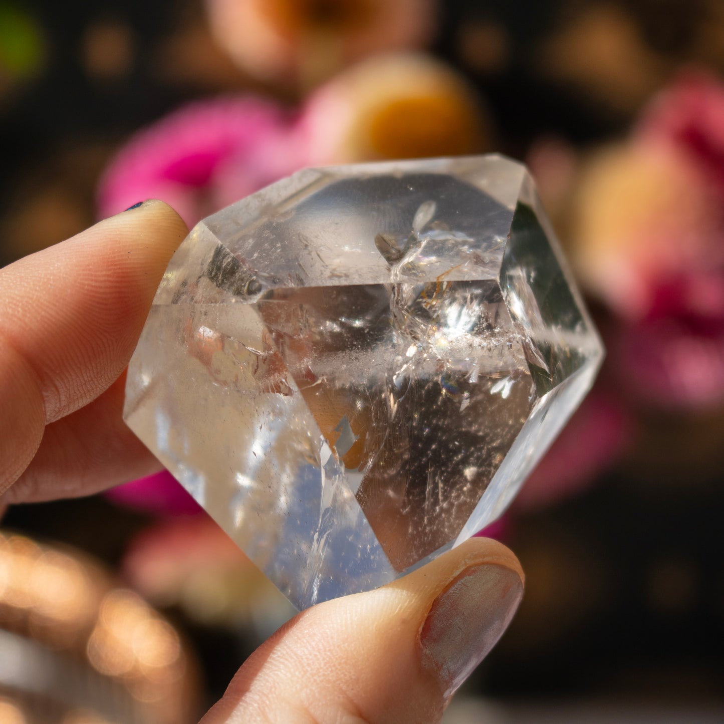 Clear crystal held by a hand with a blurred floral background