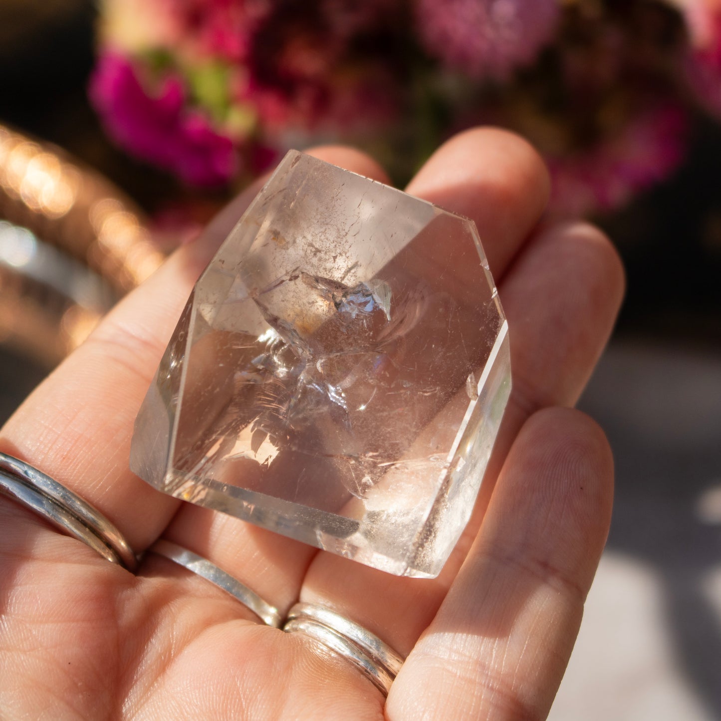 Clear crystal held in a hand with a blurred floral background
