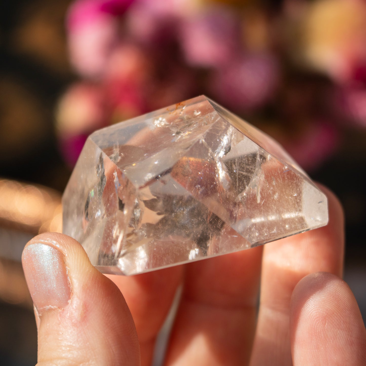 Clear crystal held in a hand with a blurred floral background