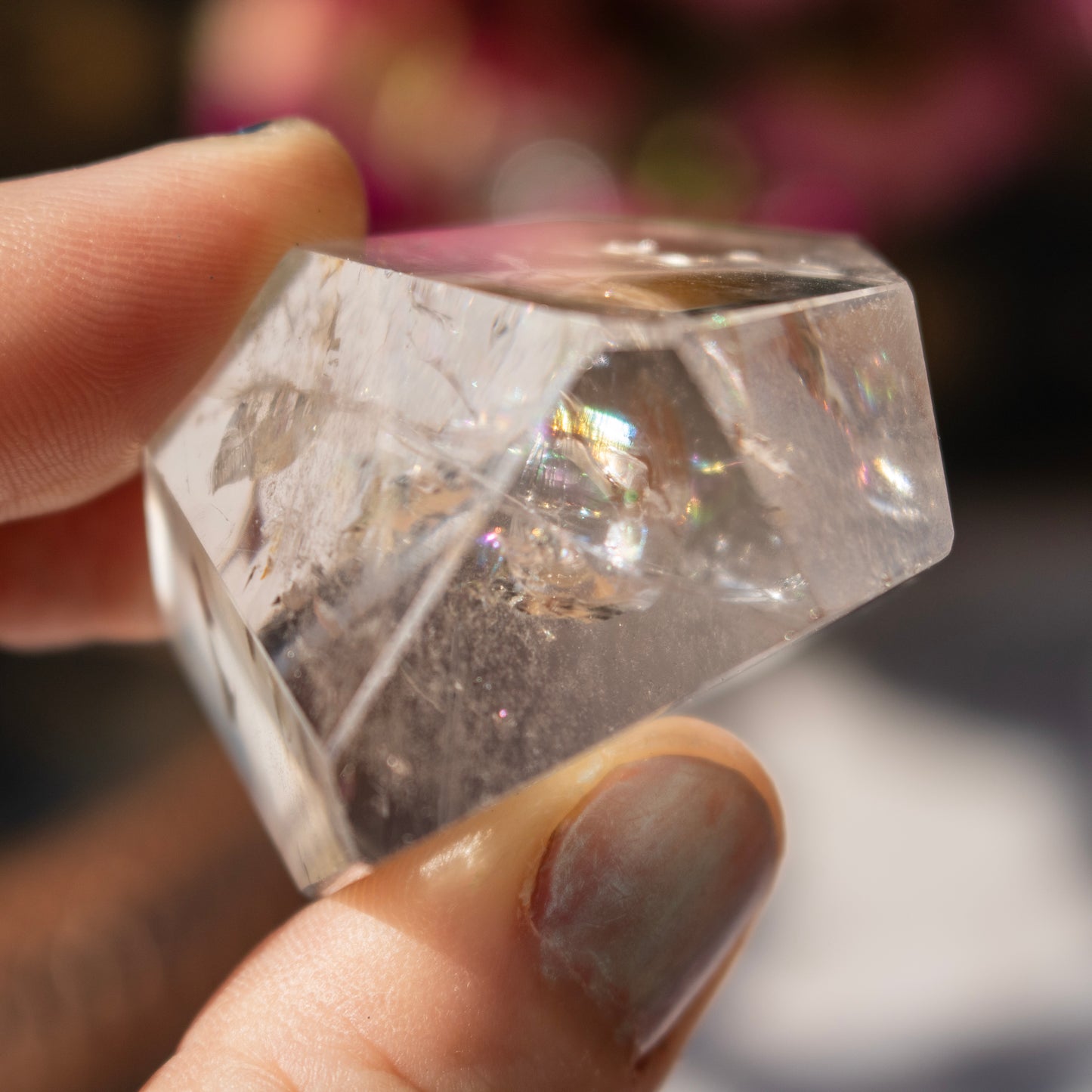 Clear stone held in a hand with flowers in the background