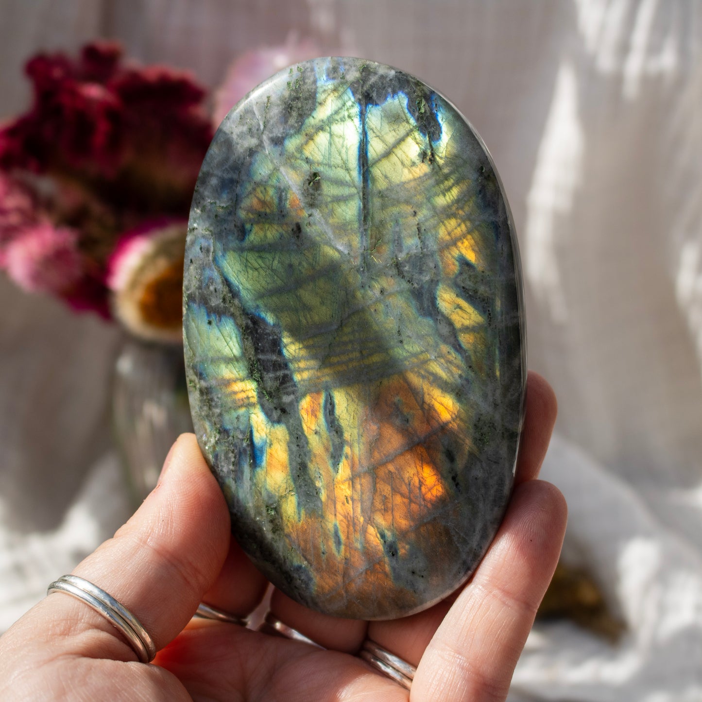 Hand holding a labradorite stone with a reflective surface, blurred background