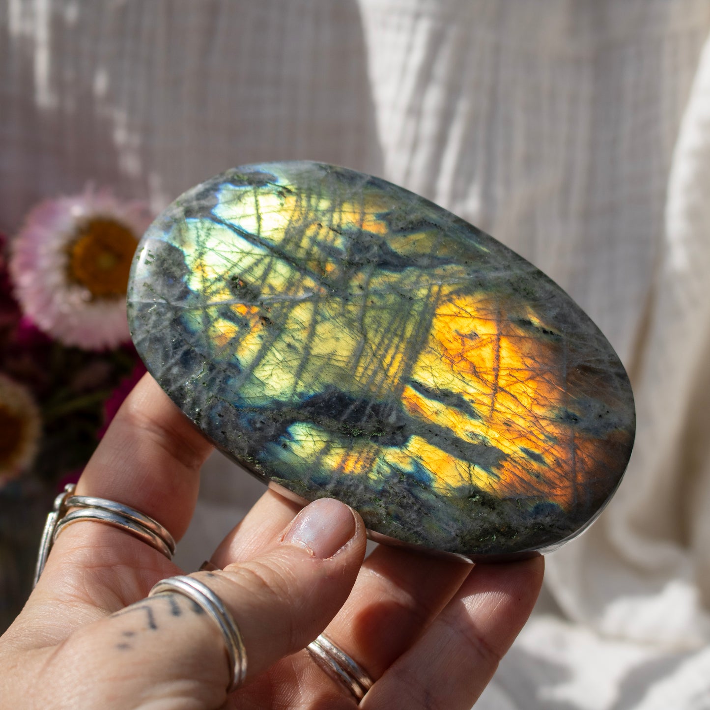Hand holding a labradorite stone with colorful reflections, blurred flowers in the background