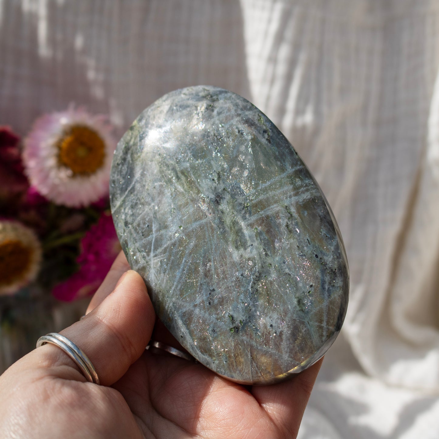 Oval-shaped stone held in a hand with a blurred floral background