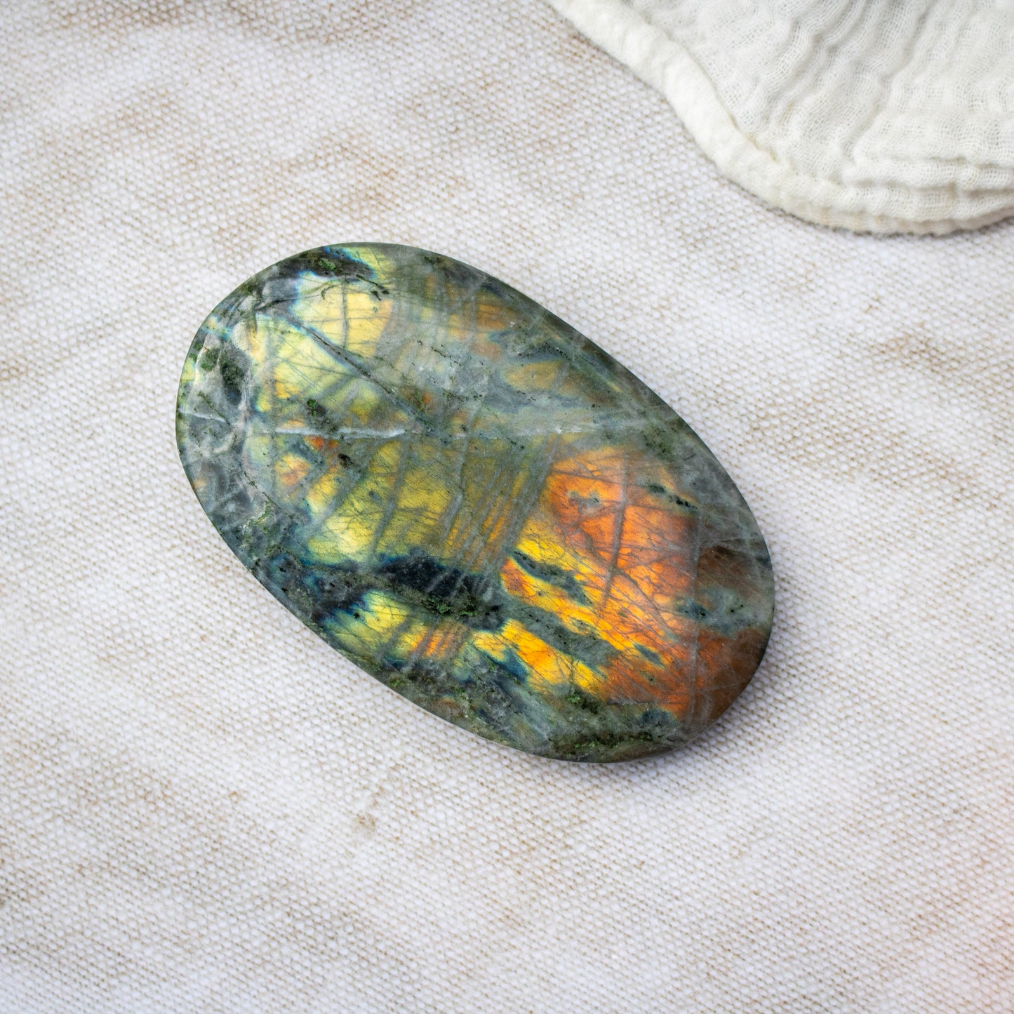 Oval-shaped labradorite stone on a textured beige surface