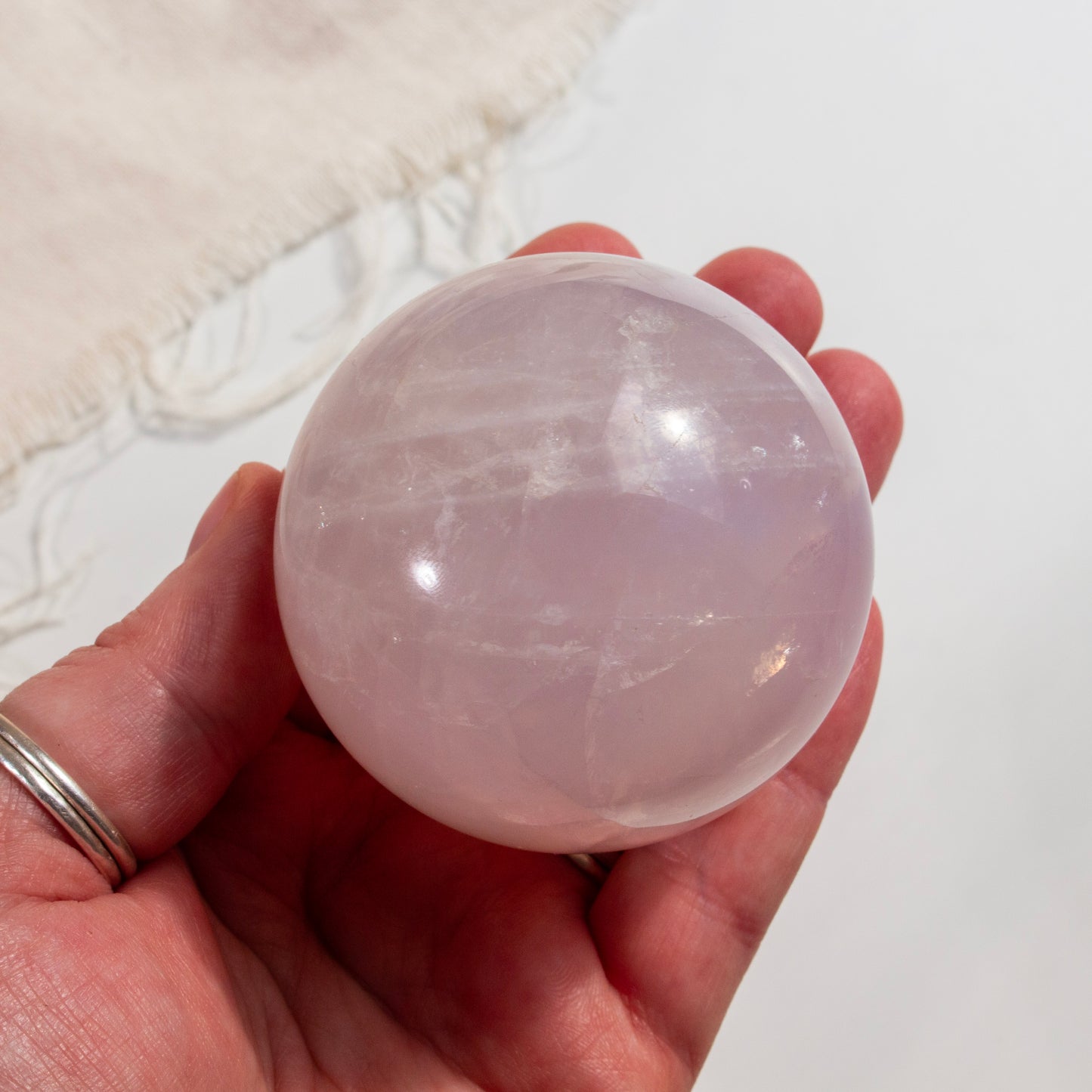 Hand holding a pink crystal sphere against a neutral background