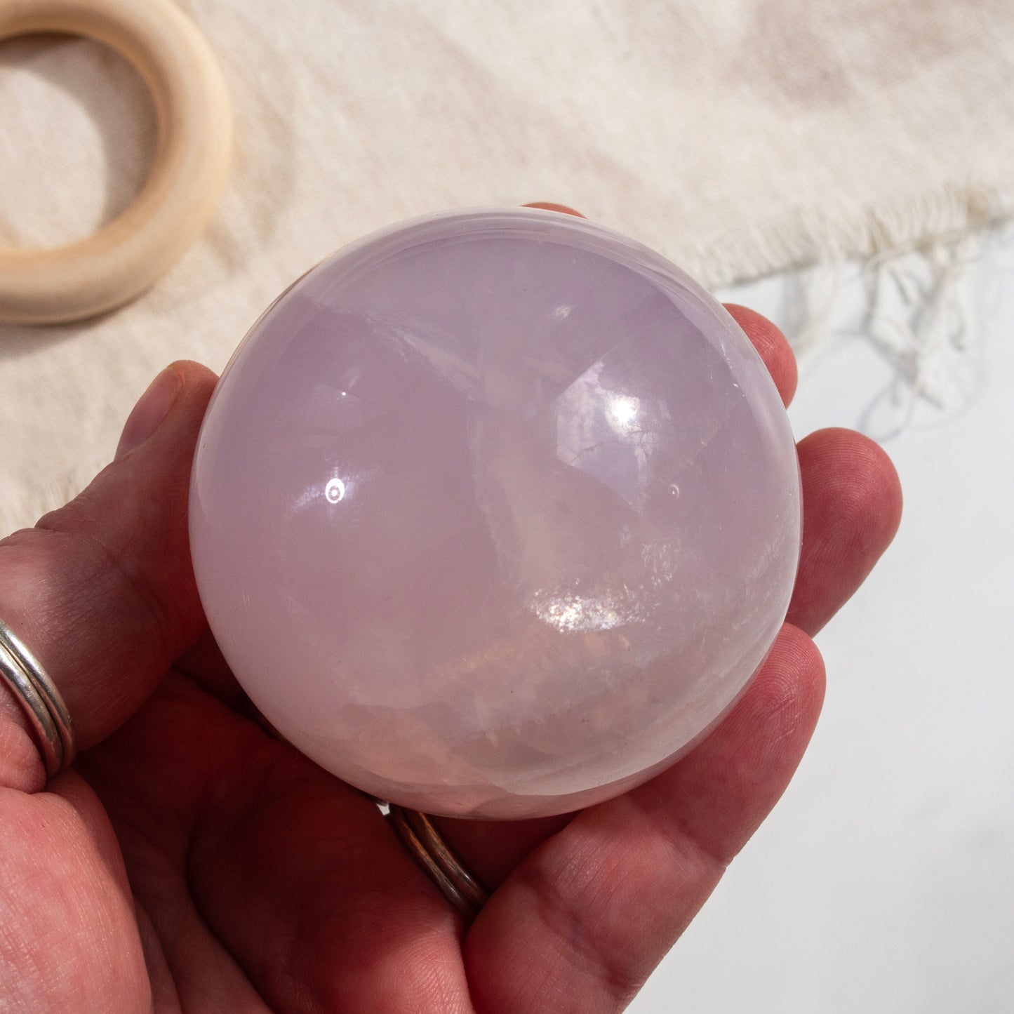 Hand holding a translucent pink crystal ball with a blurred background