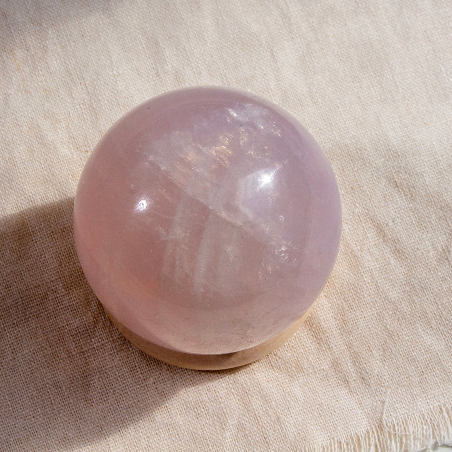 Rose quartz crystal sphere on a textured beige surface