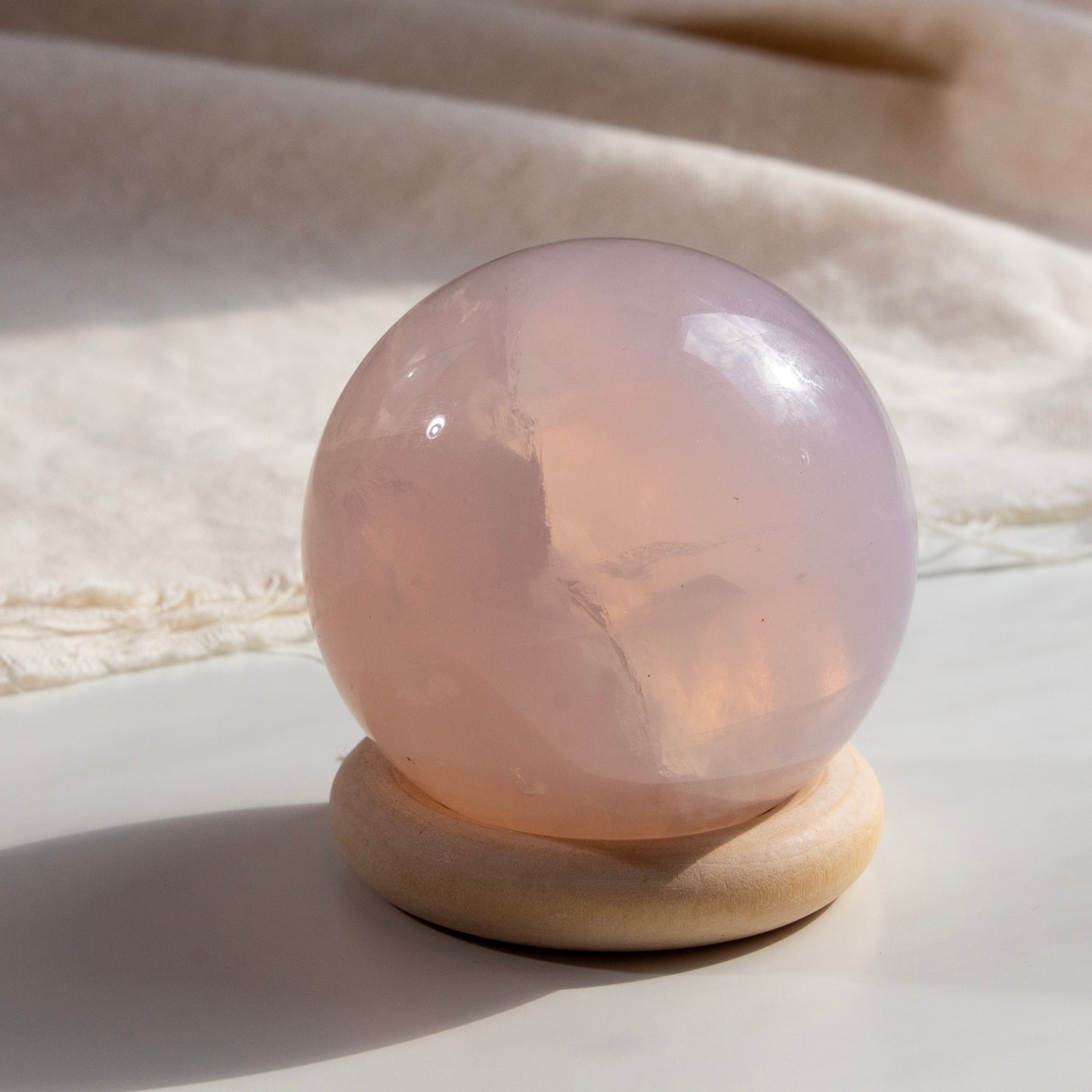 Rose quartz crystal ball on a wooden stand with a soft beige background
