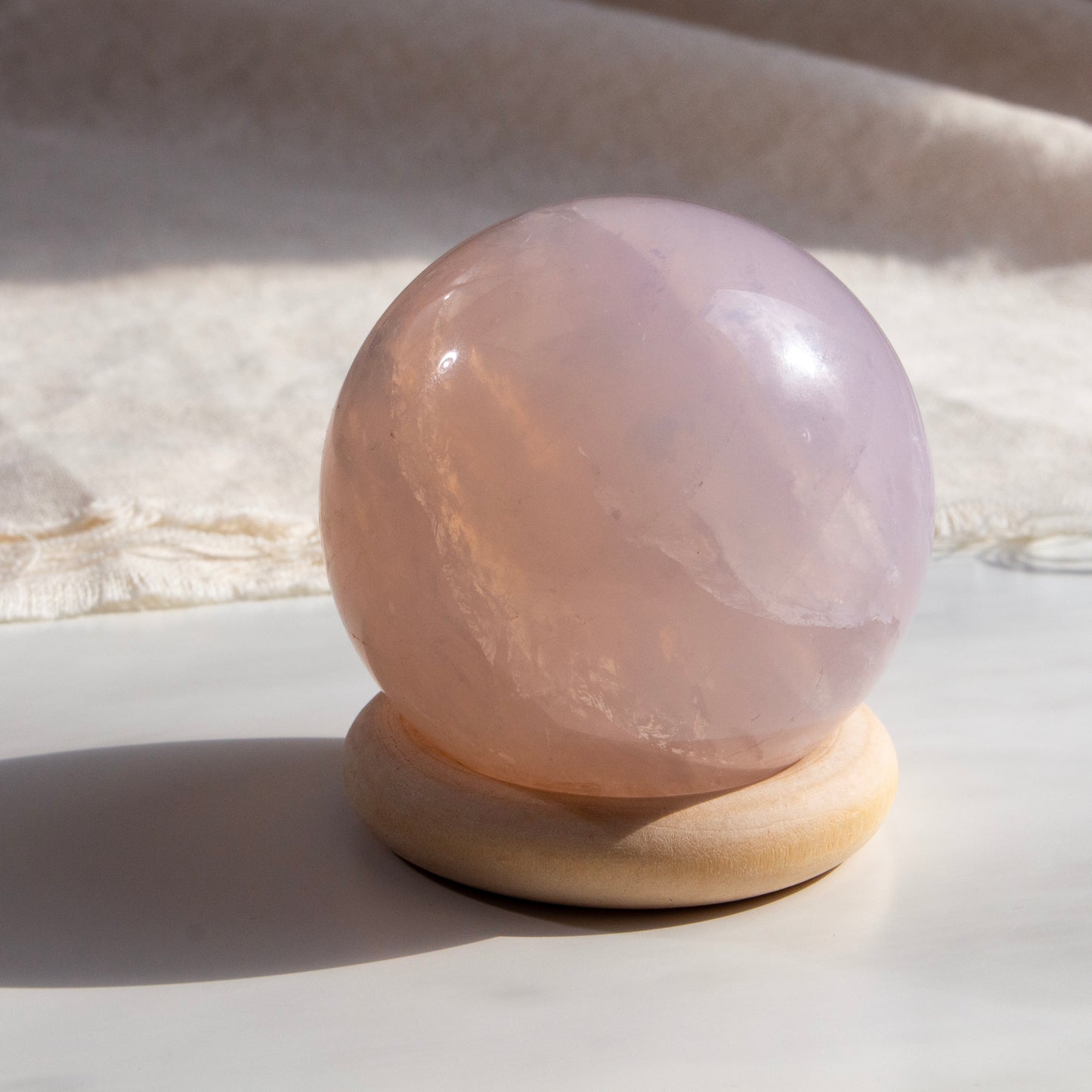 Rose quartz crystal ball on a wooden stand with a soft background