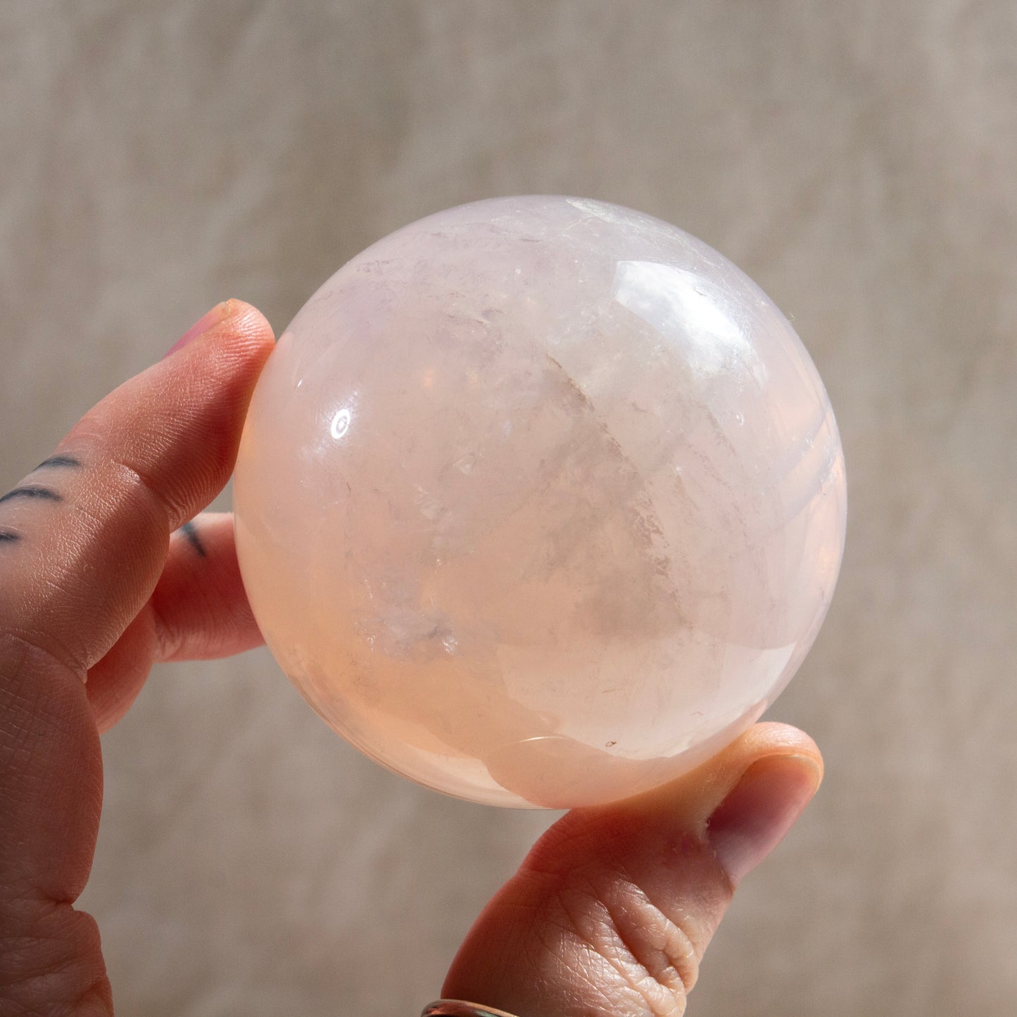 Hand holding a pink crystal sphere against a neutral background