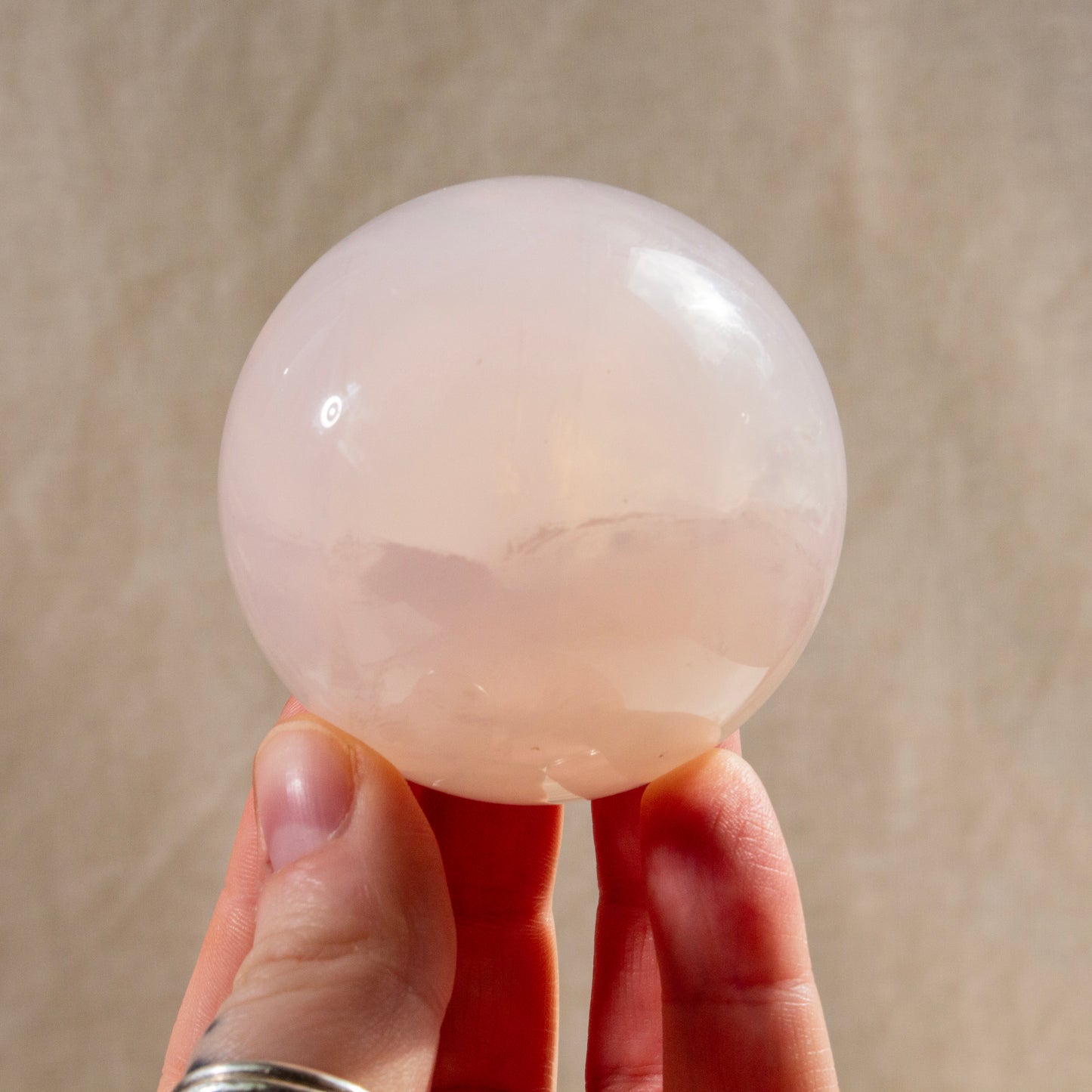 Hand holding a large pink crystal sphere against a beige background
