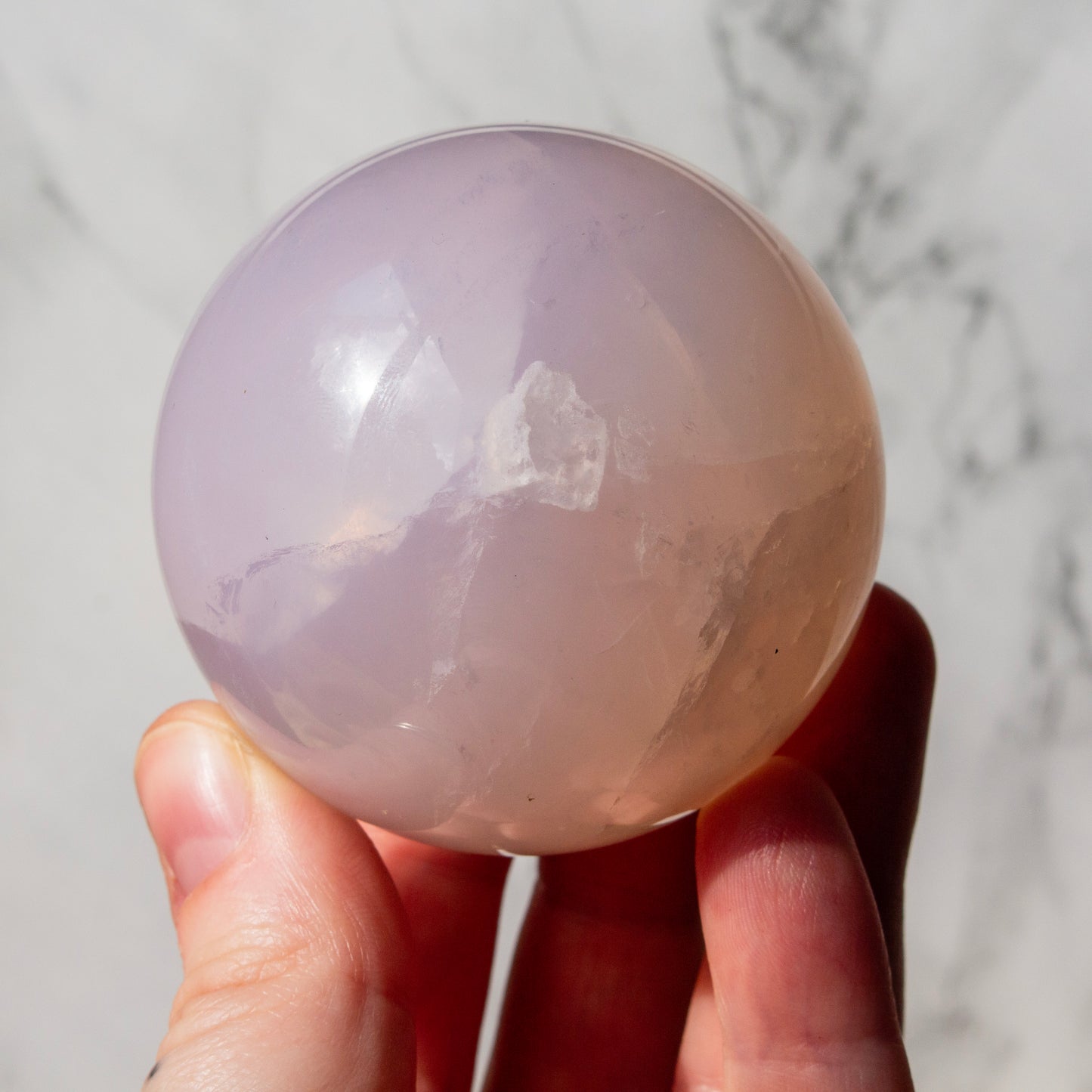 Hand holding a pink crystal ball against a marble background