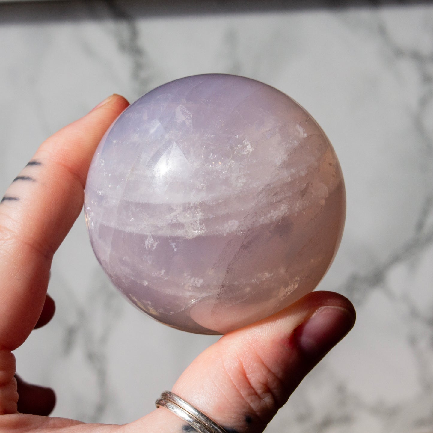 Hand holding a purple crystal ball against a marble background