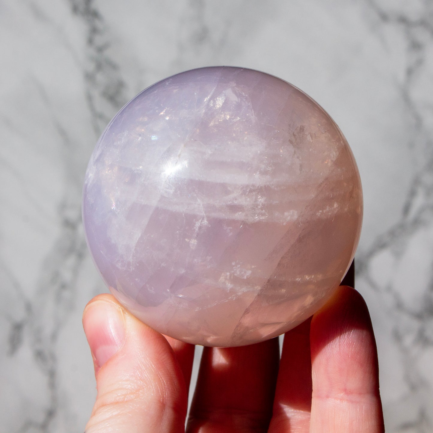 Hand holding a purple crystal ball against a marble background