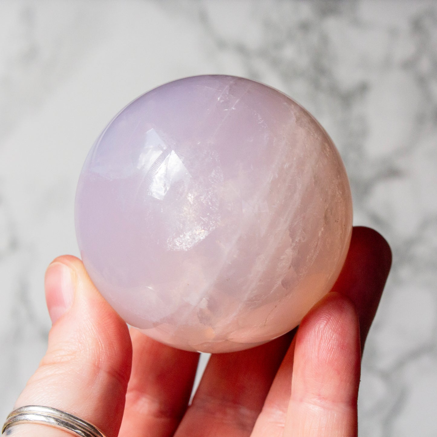 Hand holding a large, smooth, light purple crystal ball against a marble background