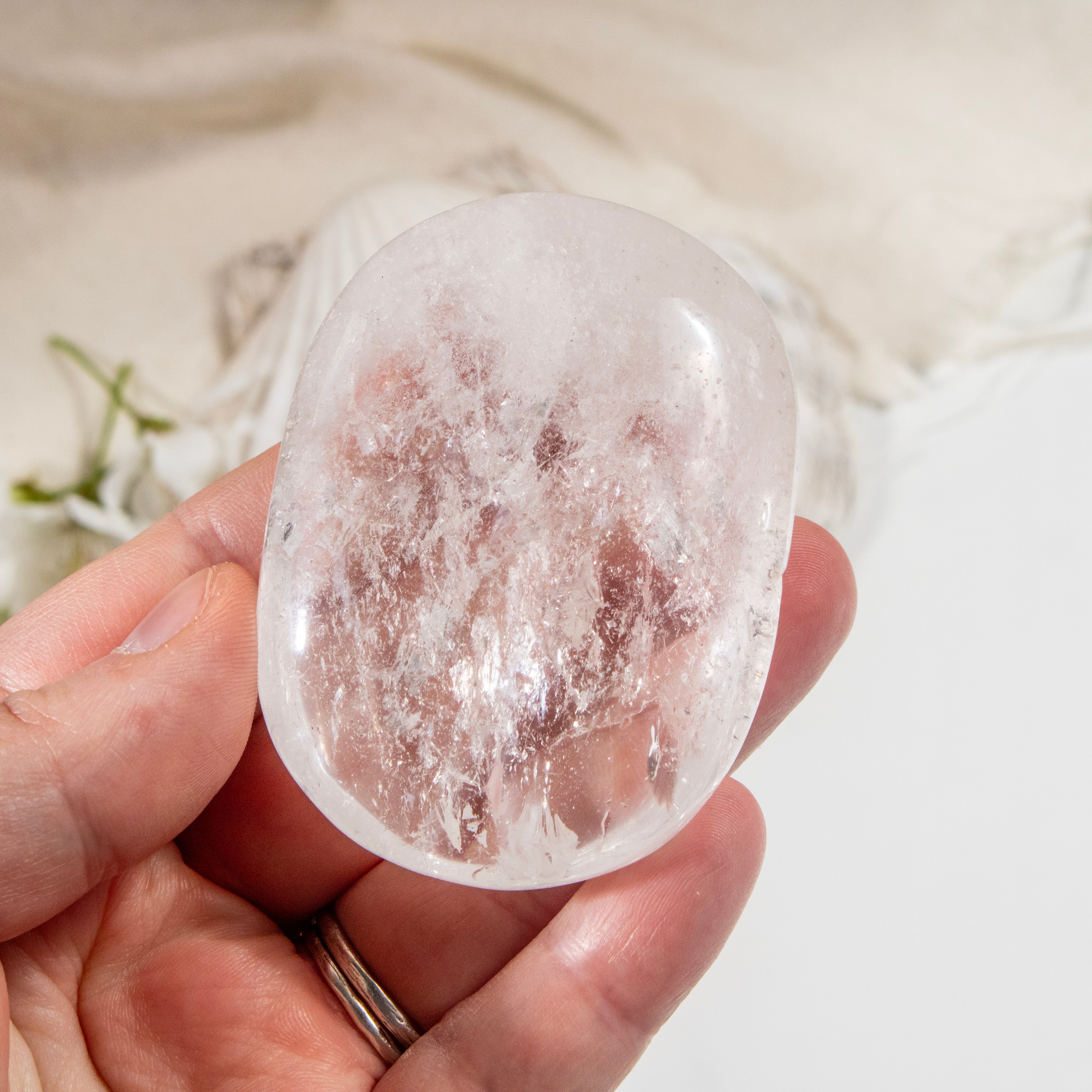 Clear crystal stone held in a hand with a blurred natural background