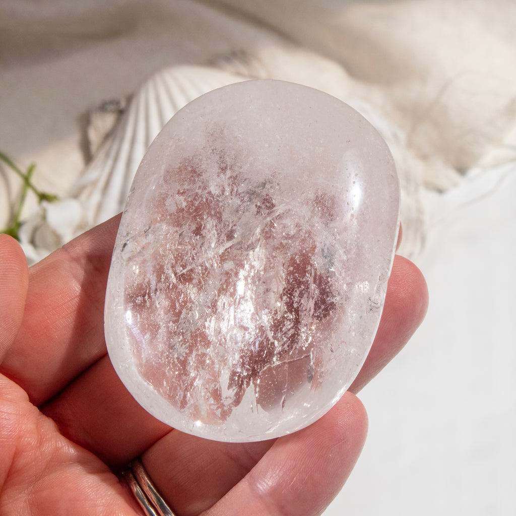 Clear crystal stone held in a hand with a natural background