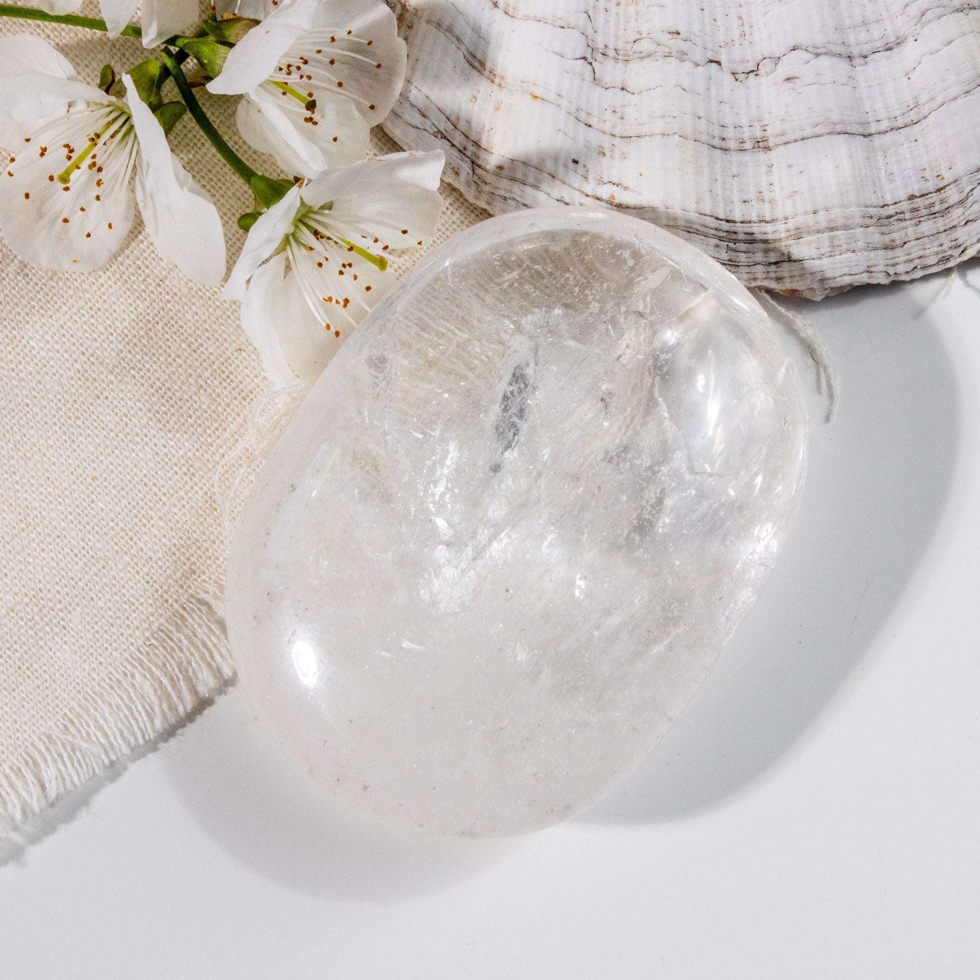 Clear crystal ball on a white surface with white flowers and a textured fabric in the background