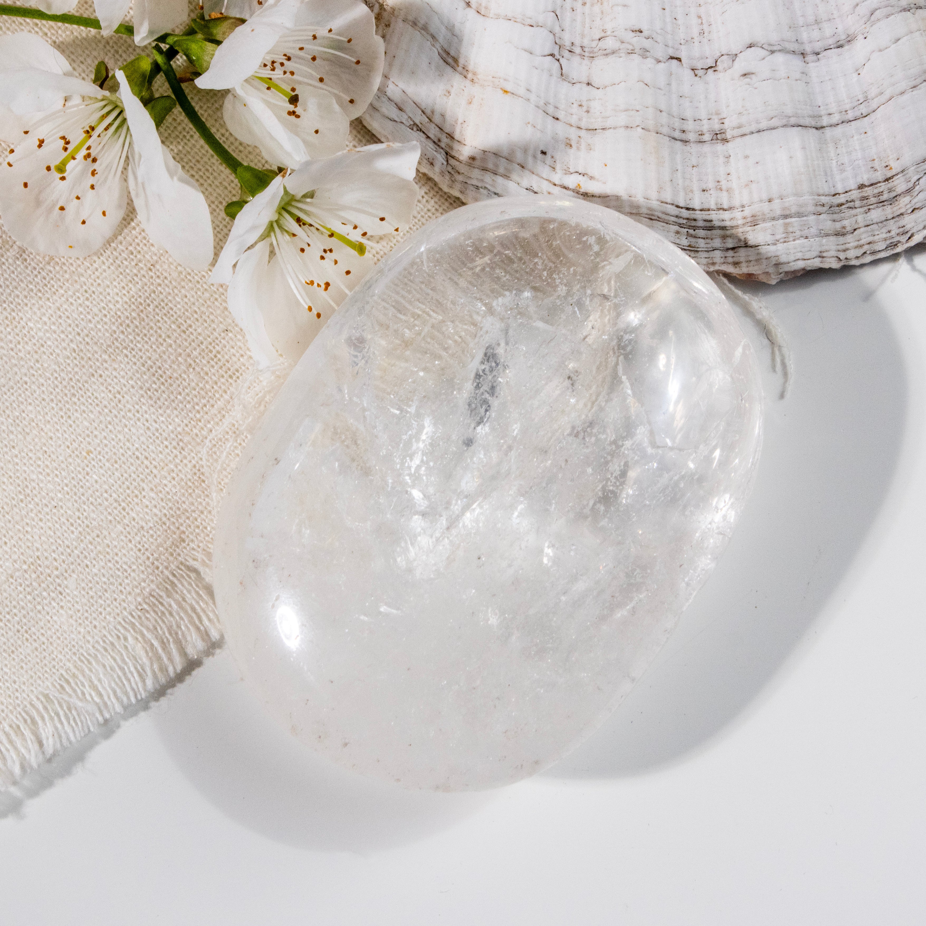 Clear crystal ball on a white surface with white flowers and a textured fabric in the background