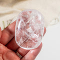 Clear crystal stone held in a hand against a neutral background