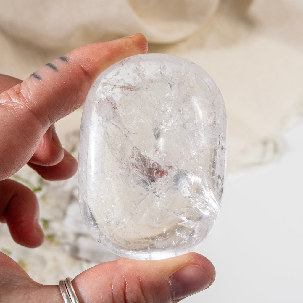 Clear crystal held by a hand against a neutral background