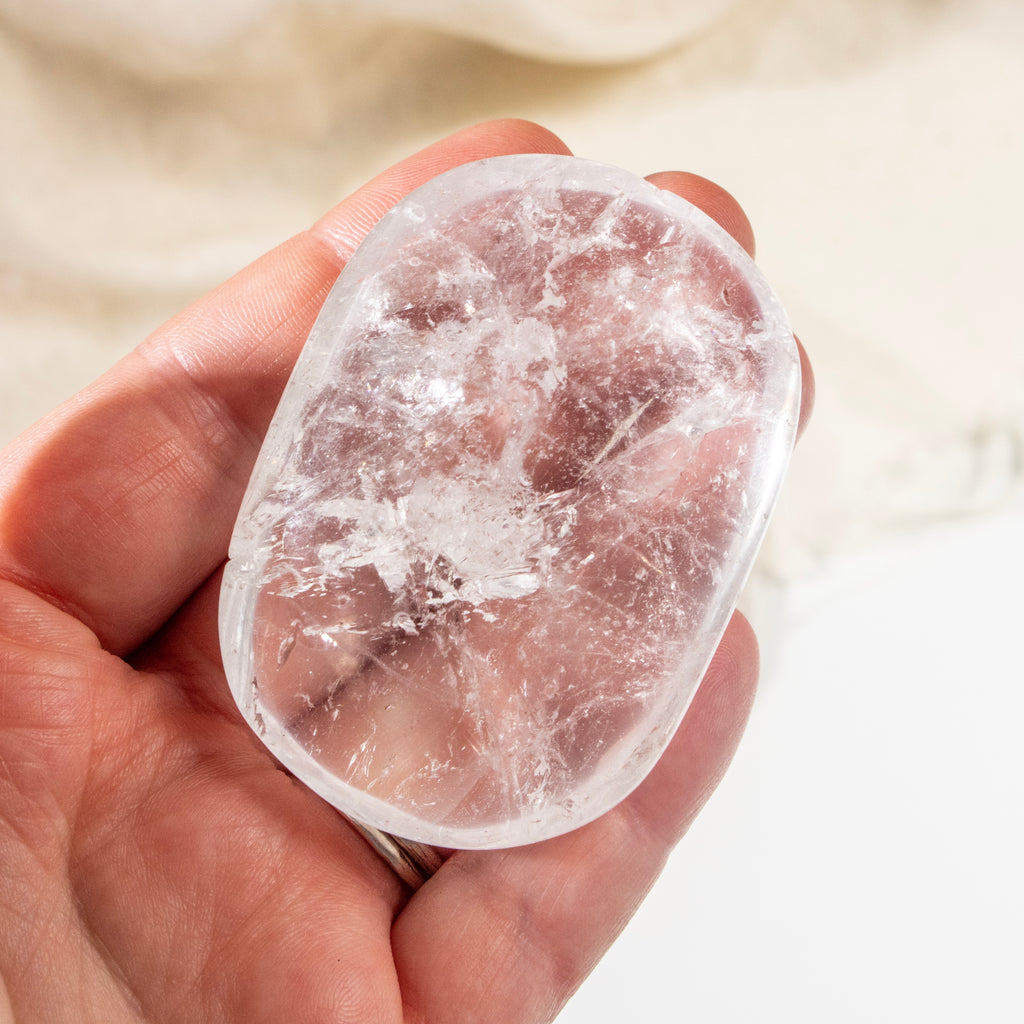 Clear crystal stone held in a hand against a neutral background
