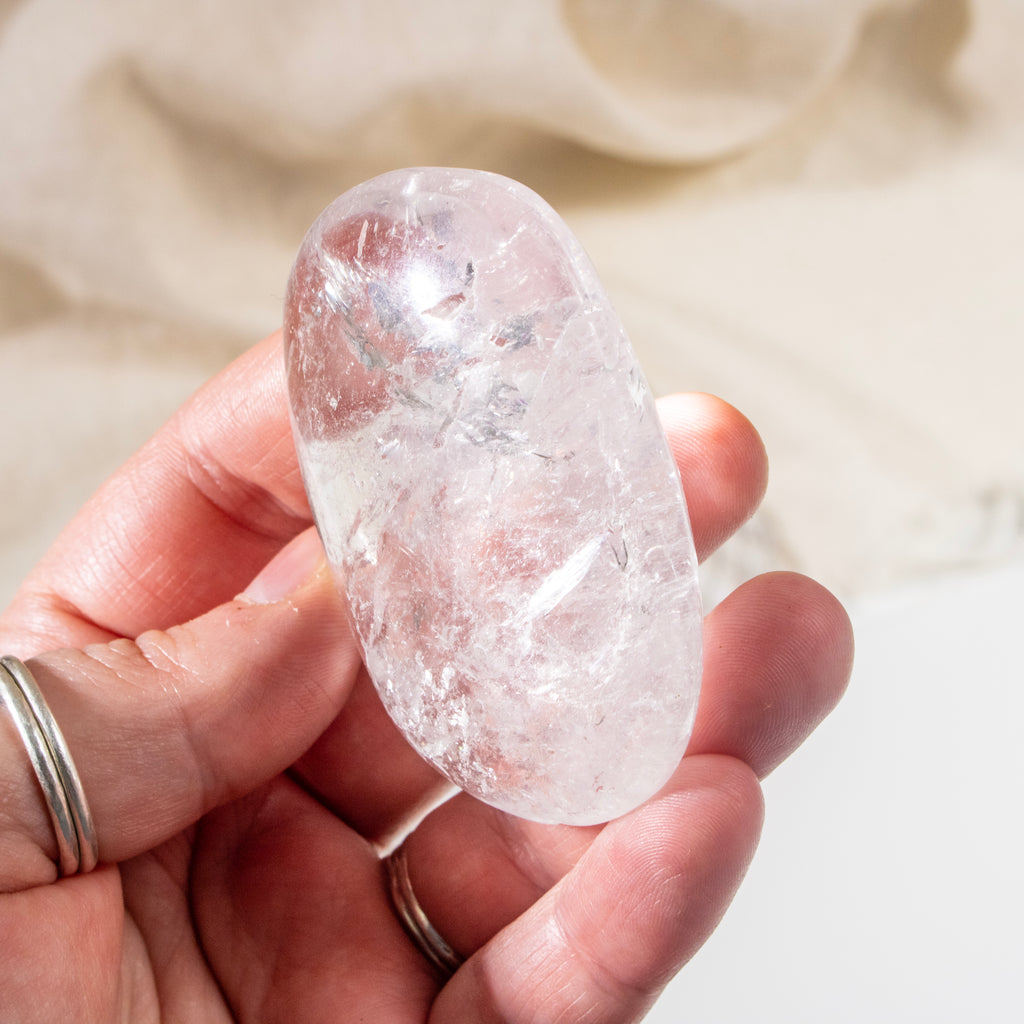 Hand holding a clear crystal stone against a neutral background