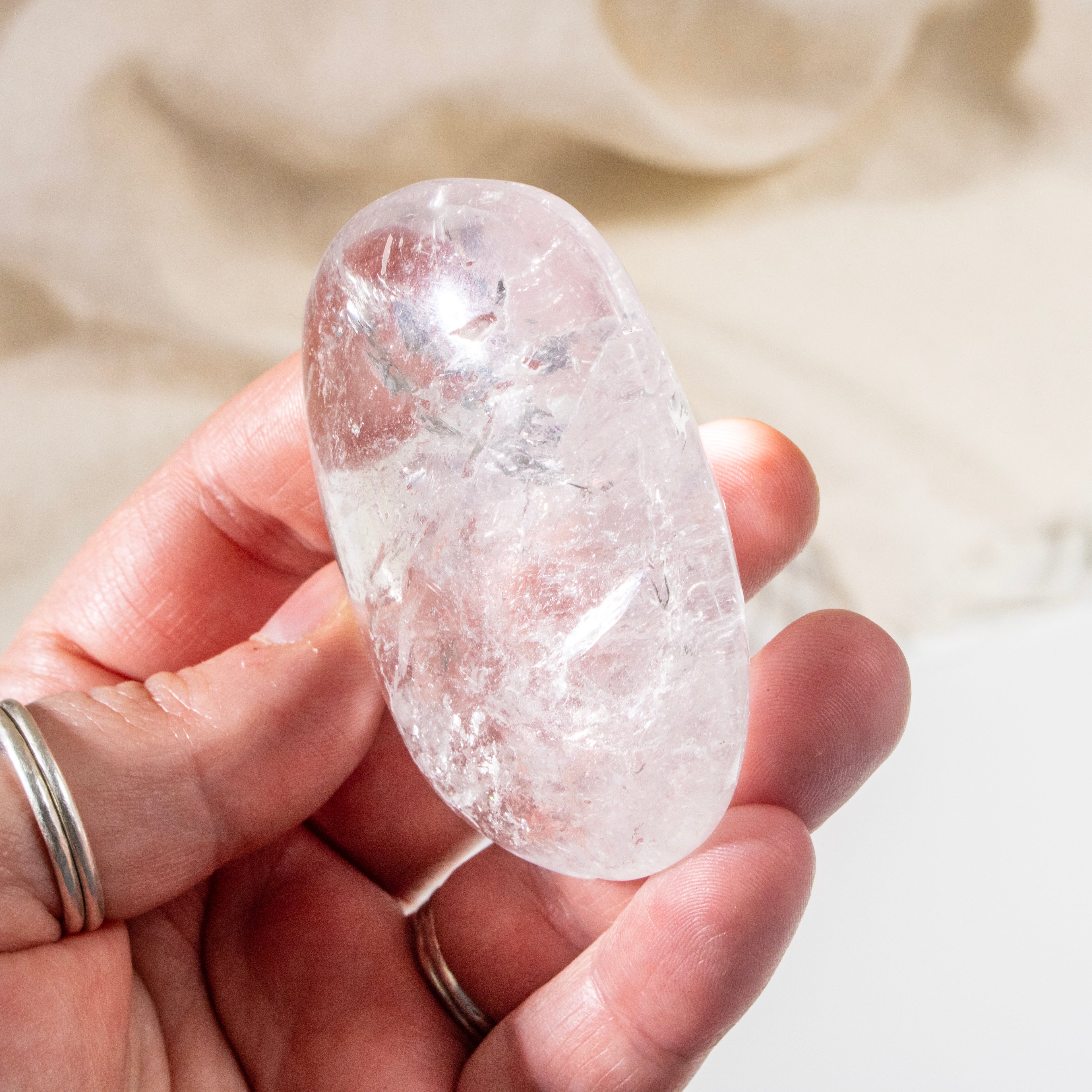 Hand holding a clear crystal stone against a neutral background