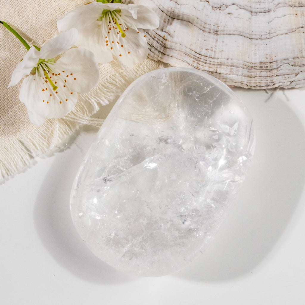 Clear crystal stone on a white surface with white flowers and fabric in the background