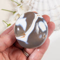 Hand holding a semi-precious stone with a marbled pattern against a blurred natural background