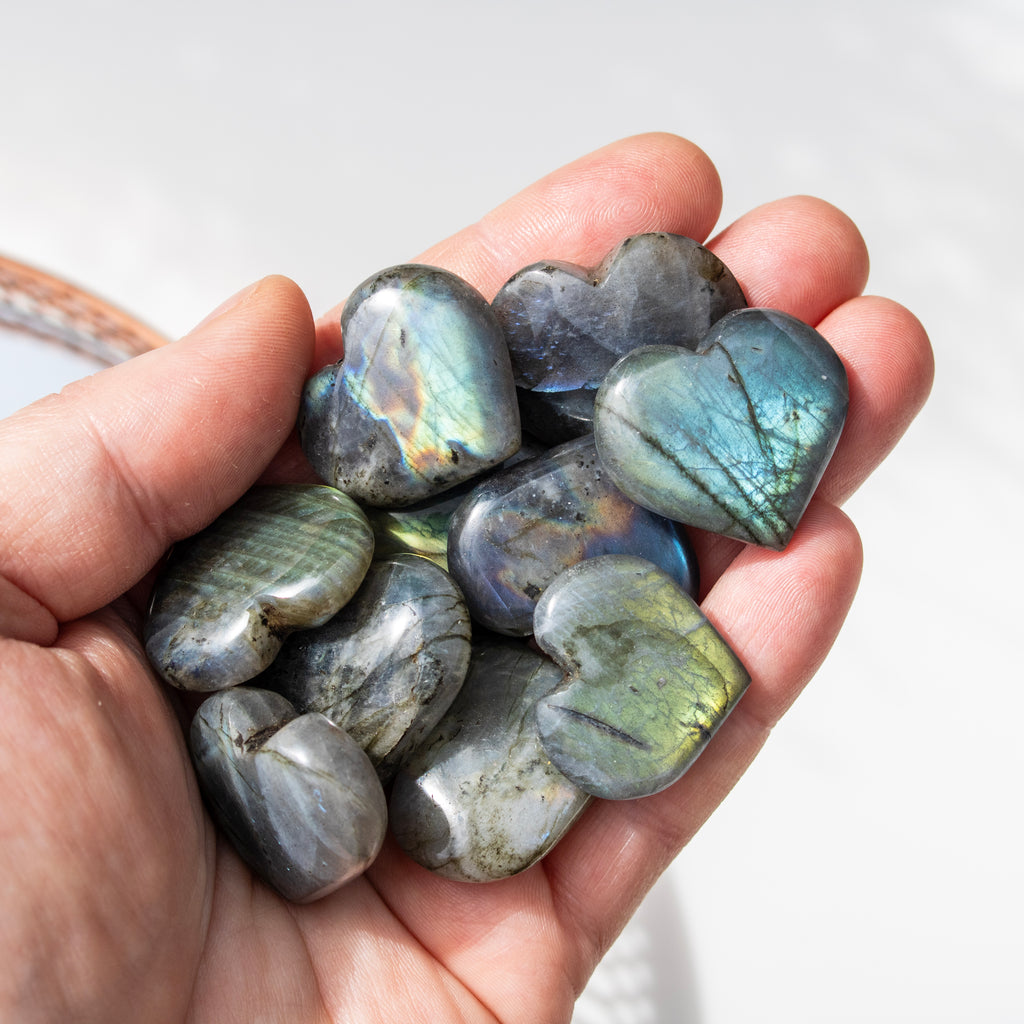 Hand holding heart-shaped Labradorite stones with a soft white background