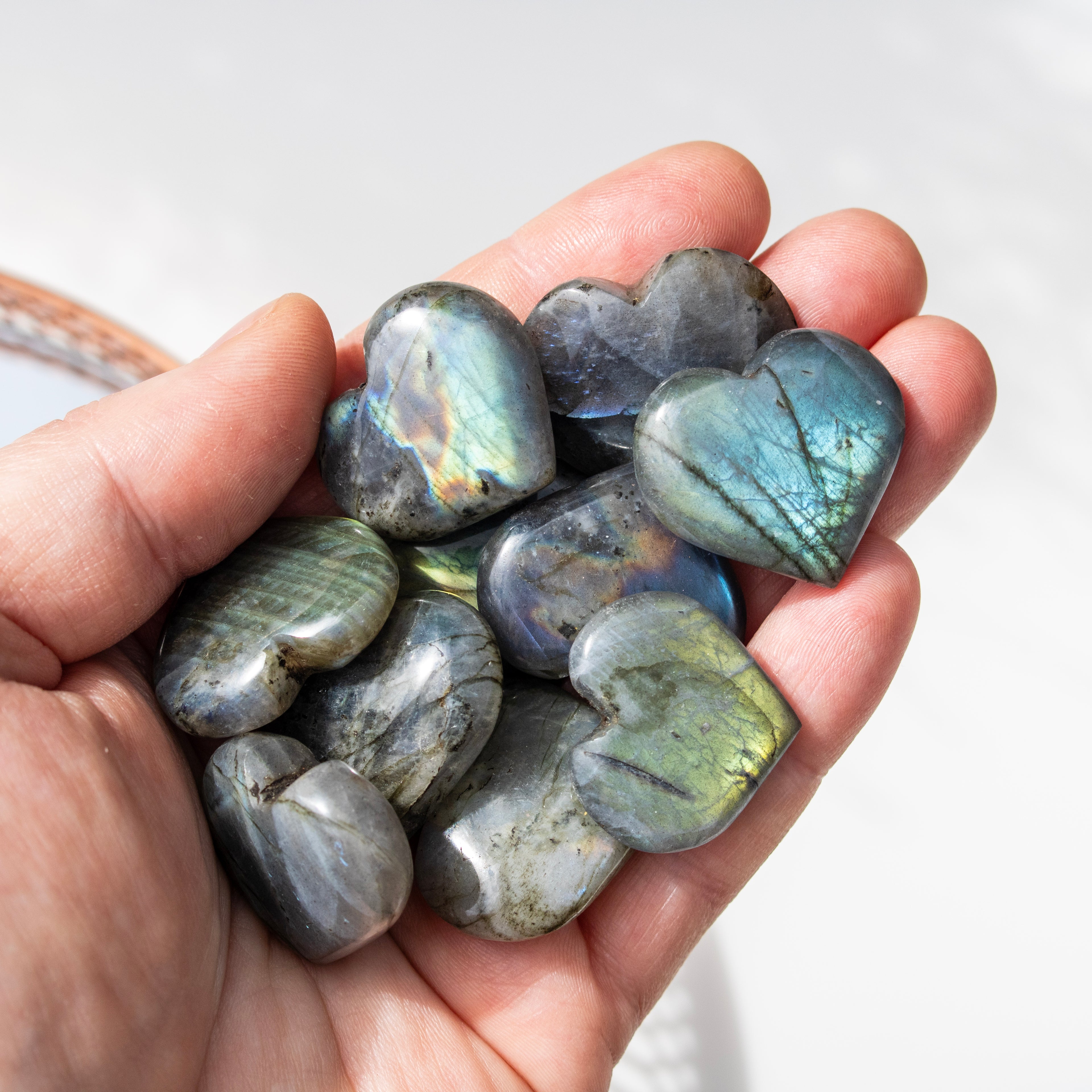 Hand holding heart-shaped Labradorite stones with a soft white background