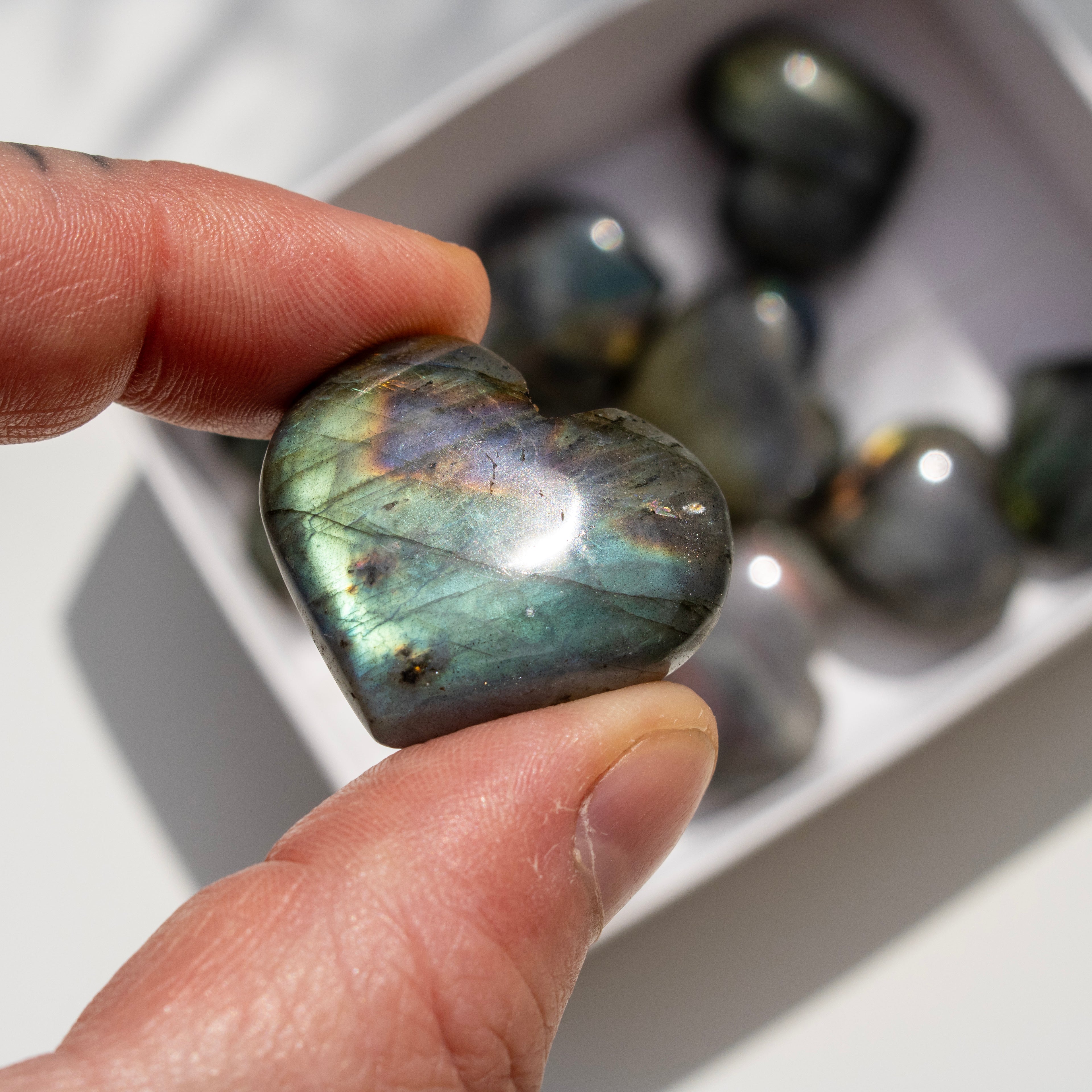 Heart-shaped labradorite stone held between fingers with more stones in the background