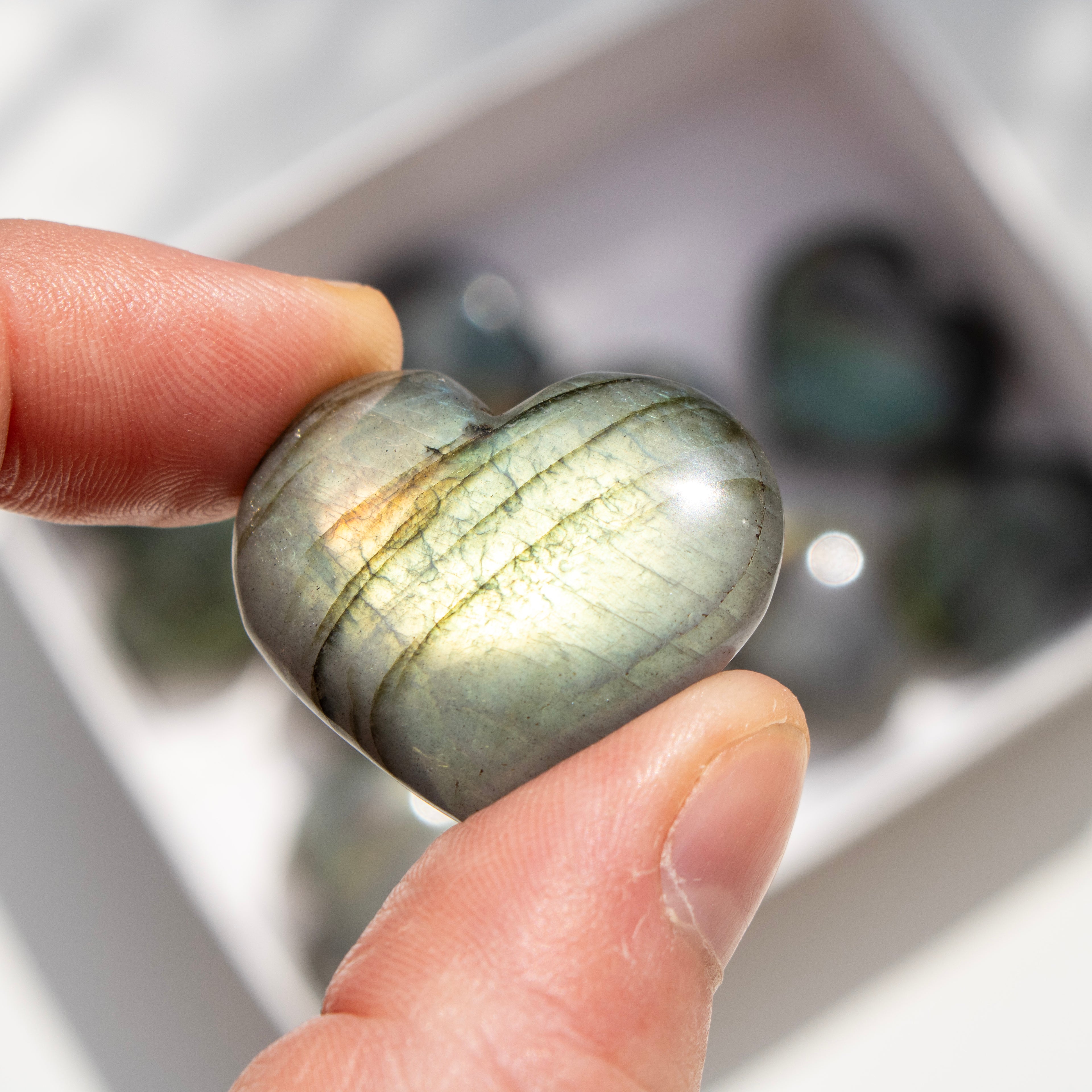 Heart-shaped labradorite stone held between fingers with a blurred background