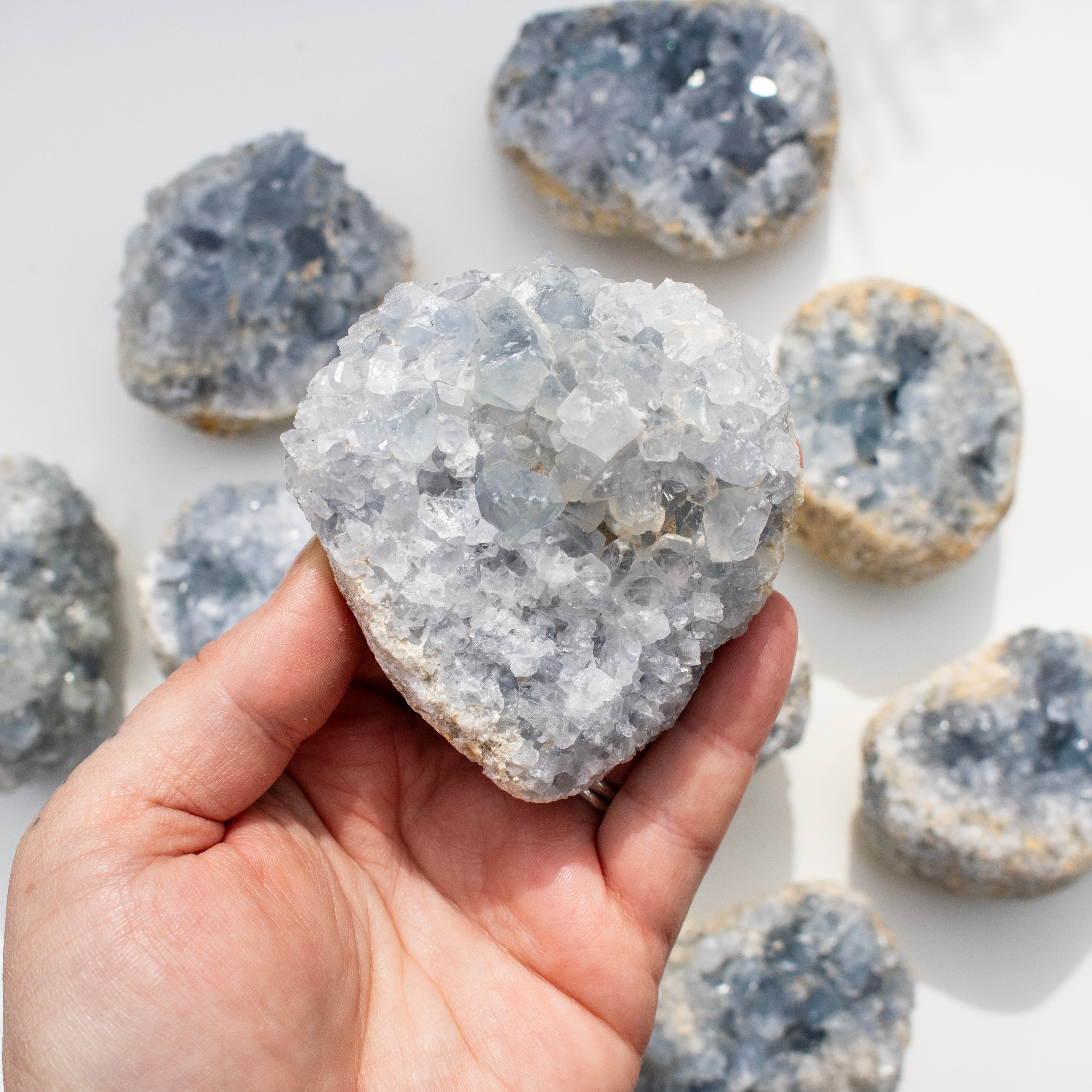Hand holding a crystal rock with more crystals in the background on a white surface