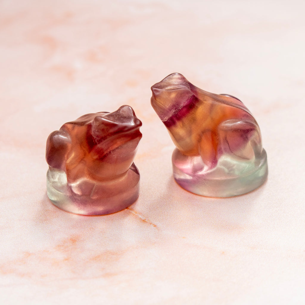 Two fluorite frog figurines on a light marble surface
