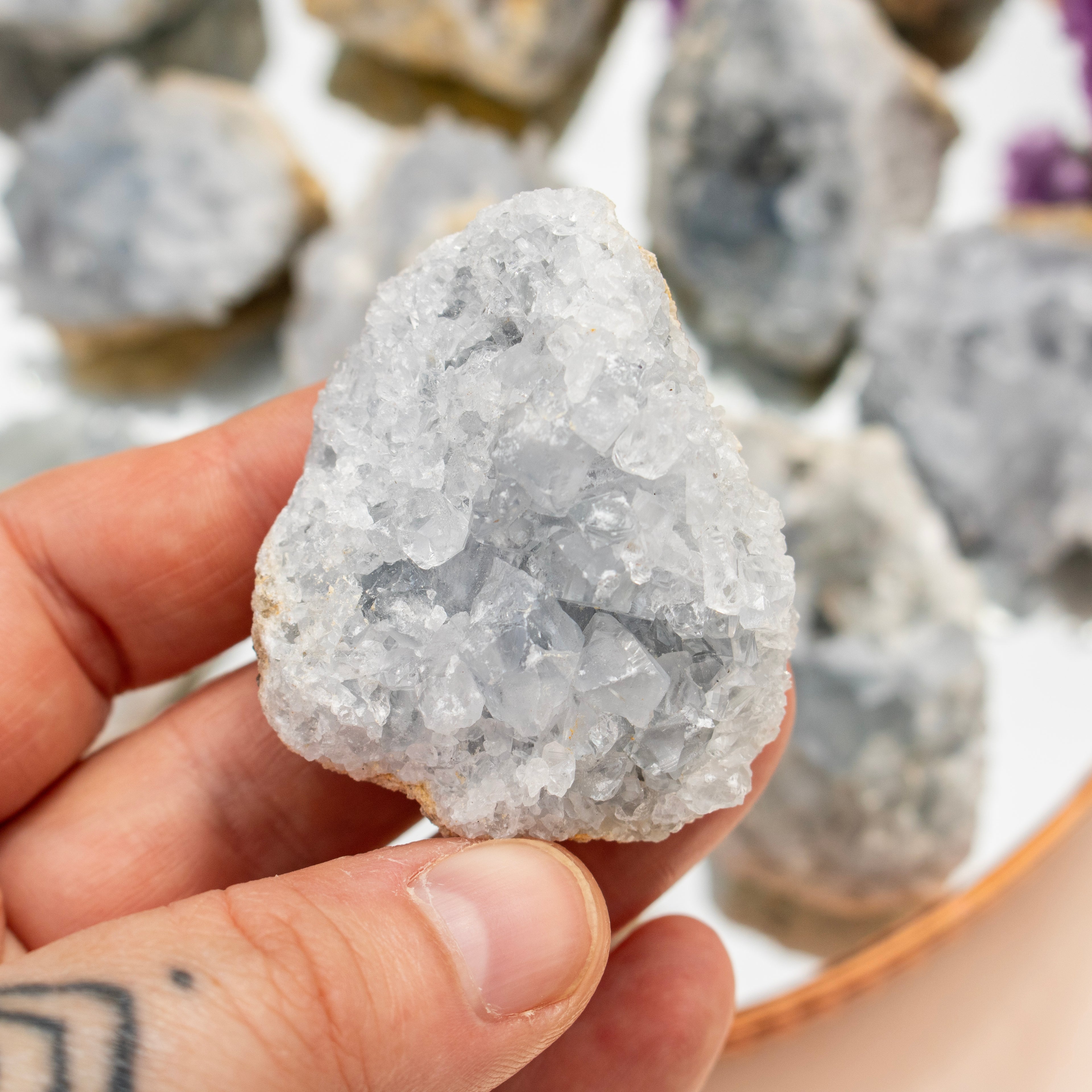 Hand holding a crystal rock with more crystals in the background