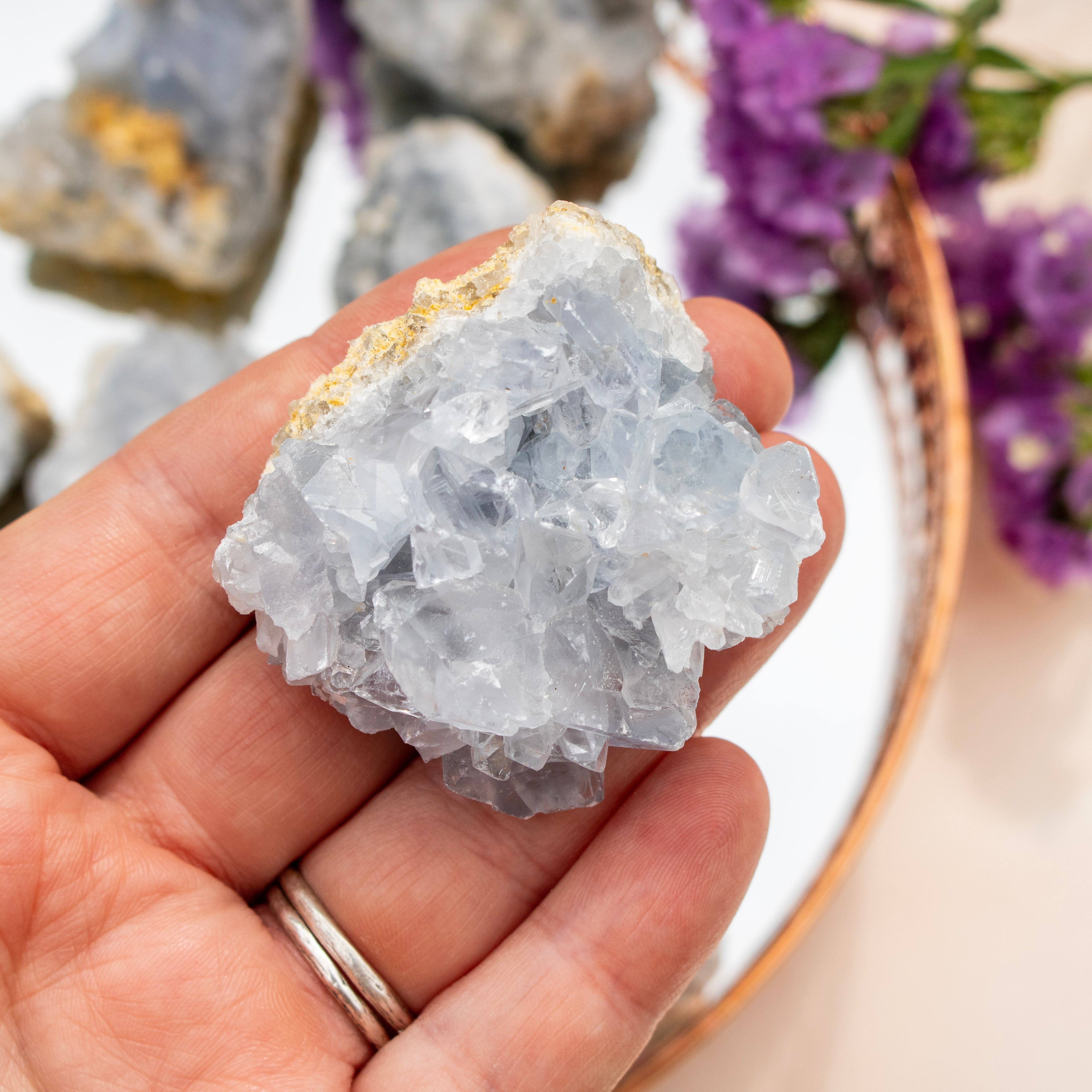 Hand holding a crystal rock with blurred purple flowers in the background