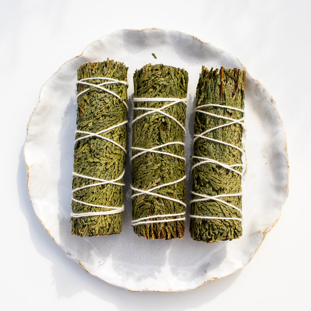 Three green cedar smudge sticks on a white plate with a white background